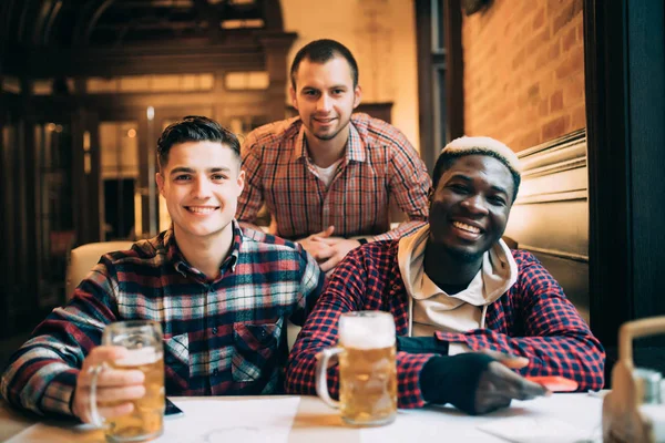 多民族の友人グループ飲んだりパブでビールを乾杯します。楽しい時間を一緒に楽しんで若い人たちと友情の概念. — ストック写真