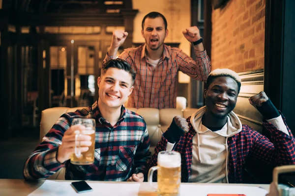 Homens multirraciais no pub regando jogo de futebol e beber cerveja . — Fotografia de Stock