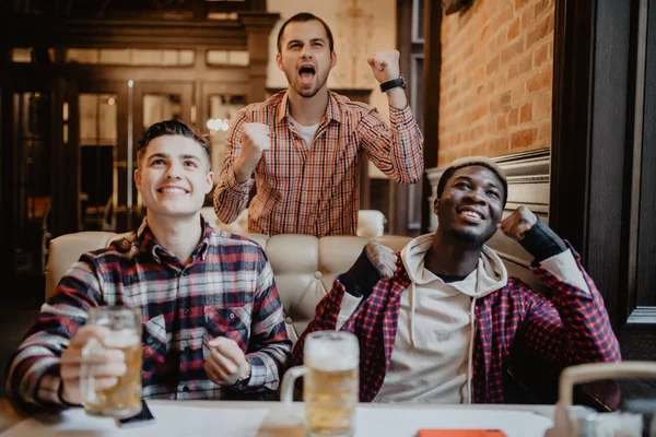 Multiracial män på pub watcing fotboll spel och dricka öl. — Stockfoto