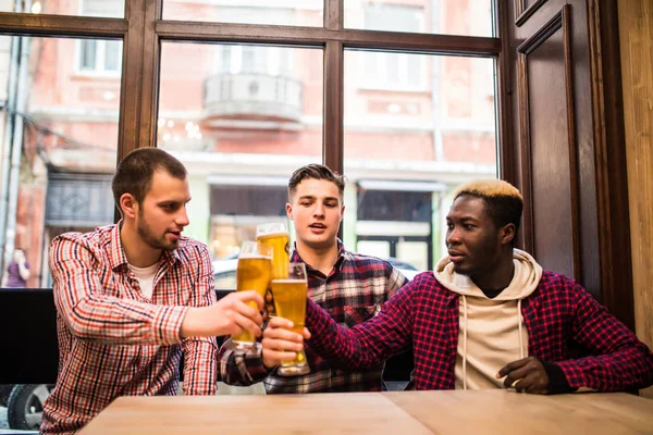 Unga lyckliga multiracial män vänner dricka öl och prata i puben — Stockfoto