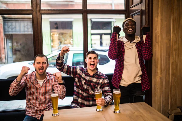 A ver televisão no pub. Jovens amigos multirraciais felizes estão torcendo por equipe e sorrindo enquanto passam tempo juntos no pub . — Fotografia de Stock
