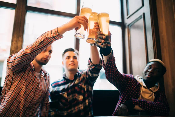 Amigos multirraciales hombres aplauden con cerveza en vasos en el pub. Brindis bar de cerveza — Foto de Stock