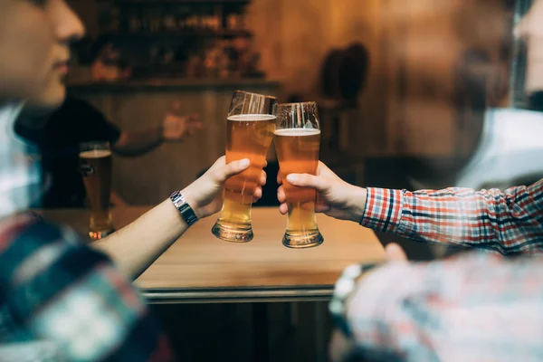 Nära håll händerna på vänner som sitter på de puben cheers med öl glasögon tråg fönster. — Stockfoto