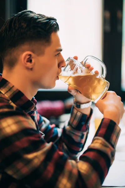 Hombre joven guapo en delantal degustación de cerveza fresca y mantener los ojos cerrados en el pub — Foto de Stock