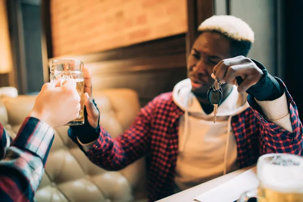 Young afro american man is holding car keys and refusing to drink beer from his friend at meet in pub. Do not drink and drive.