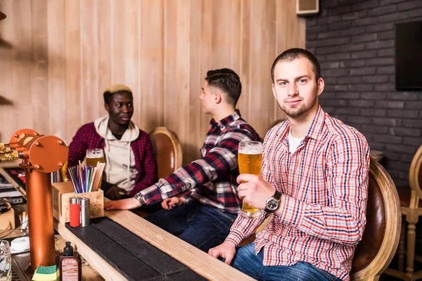 Passar tempo com os melhores amigos. Jovem bonito brindando com cerveja e sorrindo enquanto se senta com seus amigos no pub de cerveja — Fotografia de Stock