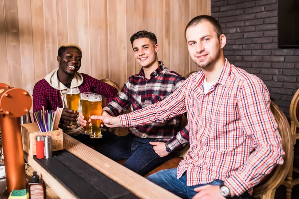 Tijd doorbrengen met beste vrienden. Knappe jongeman roosteren met bier en glimlachend zittend met zijn vrienden in bierstube — Stockfoto