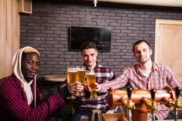 Handsome men\'s are clinking glasses of beer and smiling while resting in pub