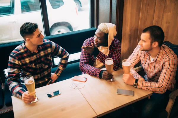 Möte med de bästa vännerna. Tre lyckliga unga män i casual wear prata och dricka öl medan du sitter i bar grupp — Stockfoto