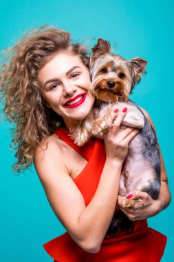 Kameraya bakarak ve Yorkshire terrier izole görünümü yeşil zemin üzerine tutarak gülümseyen genç çekici kadın portresi.