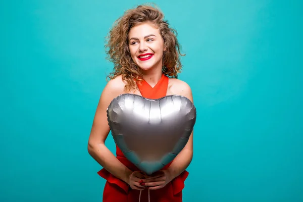 Mujer de belleza en traje rojo de lujo posando en la cámara con el balón en forma de corazón, aislado sobre la pared verde — Foto de Stock