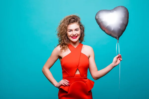 Mujer de belleza en traje rojo de lujo posando en la cámara con el balón en forma de corazón, aislado sobre la pared verde — Foto de Stock