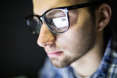 Odaklanmış ve düşünceli bir adam. Coder, programcı veya karanlıkta dizüstü kullanarak geliştirici. Geç saatlere kadar iş adamı. Geceleri öğrenci. Gözlük bilgisayar ekran yansıması ile yakın çekim.