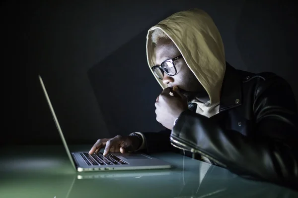 Афро-американский хакер в Худе с помощью портативного компьютера в сети Dark Hack или электронной почты аккаунт в ночное время — стоковое фото