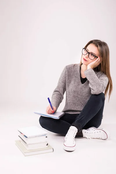 Giovane studentessa seduta sul pavimento circondata da libri, prendere appunti, prepararsi per l'esame su sfondo bianco . — Foto Stock