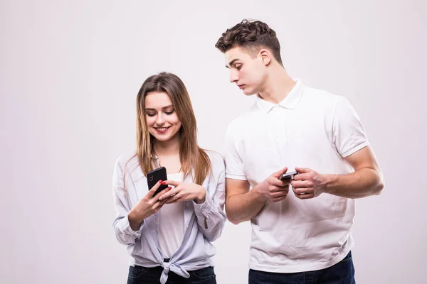Närbild porträtt av en Blandras leende par använda mobiltelefoner isolerat på den grå bakgrunden. Mannen tittar på kvinnan telefoner — Stockfoto