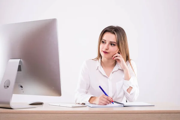 Mujer joven sentada frente a una PC en el escritorio, aislada sobre fondo blanco — Foto de Stock