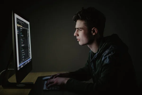 Концепция разработки программы. Молодой человек, работающий с компьютером в темной комнате . — стоковое фото