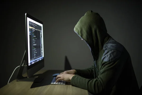 A hacker in a hood on a dark background hacking computer networks in dark room — Stock Photo, Image