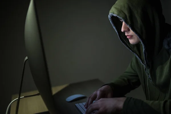 A hacker in a hood on a dark background hacking computer networks in dark room — Stock Photo, Image