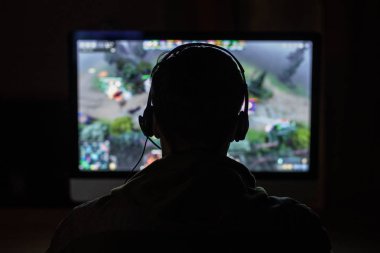 Arkadan görünüşü konsantre genç oyun kulaklıklar ve bilgisayarla oynamak için gözlük karanlık evde oyun