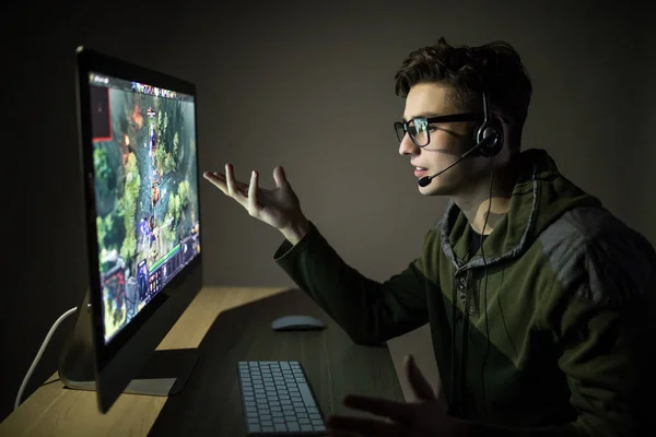 Gamer muda di headphone dan kacamata menggunakan konsol dan komputer untuk bermain game di malam hari dan gestur dengan tangan setelah kehilangan . — Stok Foto