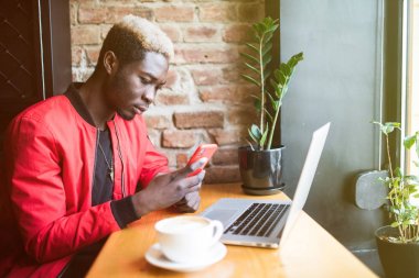 Yakışıklı Afro Amerikan önünde elinde telefon ile kafeteryada oturan adam dizüstü bilgisayar, klavye ve internet, kahve içme arama açıldı. Classe için hazırlanıyor esmer genç erkek öğrenci