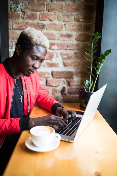 Porträt eines afrikanisch-amerikanischen Mannes, der in einem Café sitzt und an einem Laptop arbeitet. — Stockfoto