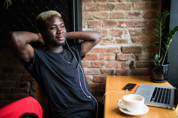 Retrato de un hombre afro americano sonriente sentado en la cafetería con las manos detrás de la cabeza delante de la computadora portátil relajarse en la cafetería — Foto de Stock