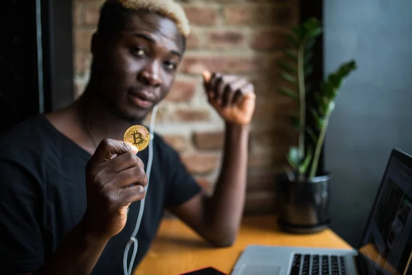 Afro Αμερικανός νεαρός με bitcoin στο χέρι στο μέτωπο του lap-top στο καφέ — Φωτογραφία Αρχείου