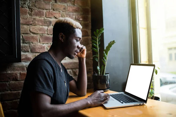 Retrato lateral de un joven afroamericano trabajando portátil con pantalla blanca para espacio de copia en la cafetería — Foto de Stock
