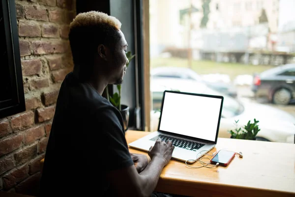 Vista trasera de un joven estudiante africano que trabaja en la computadora portátil mientras toma un café en la cafetería — Foto de Stock