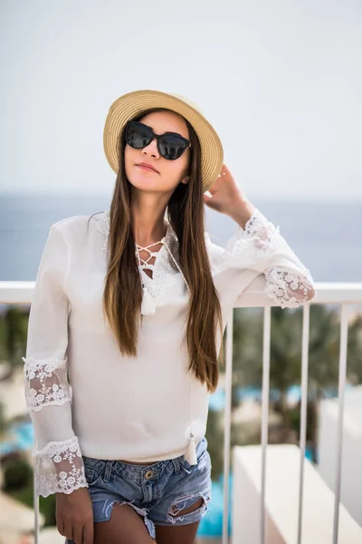 Hermosa mujer en sombrero de paja y gafas de sol de lujo relajante en la terraza del hotel disfrutando del sol en el cielo azul del mar al aire libre fondo —  Fotos de Stock