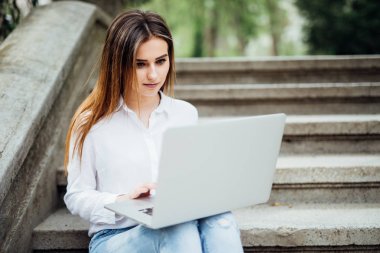 Geri kalan üniversite kampüsü içinde sahip laptop ile çalışma, açık havada, sınavlara hazırlanma merdivenlerde oturan öğrenci kız gülümsüyor. Teknoloji, eğitim ve uzak çalışma kavramı, kopya alanı