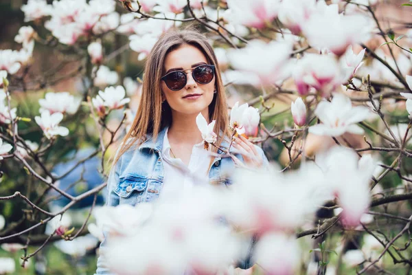 Portréja egy fiatal gyönyörű nő közelében magnólia fát, virágok. — Stock Fotó