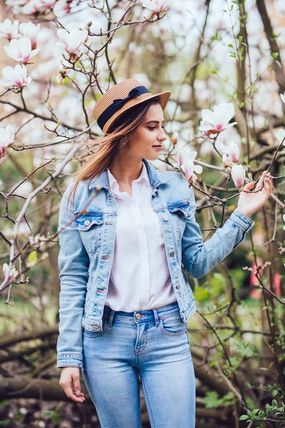 Ritratto di giovane bella donna in cappello di paglia in alberi di fiori primaverili . — Foto Stock