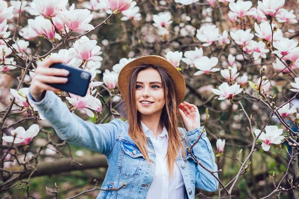 봄 꽃 정원 공원 목련 꽃에 대 한 전화에 selfie를 만드는 밀 짚 모자에 관능적인 아름다움 여자의 초상화 — 스톡 사진