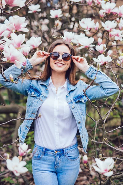 Ritratto di una giovane bella donna in occhiali da sole vicino all'albero di magnolia con fiori in fiore . — Foto Stock