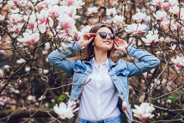 Elegante donna casual in occhiali da sole contro alberi primaverili in fiore — Foto Stock