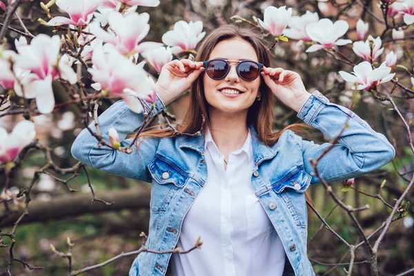 Elegante donna casual in occhiali da sole contro alberi primaverili in fiore — Foto Stock