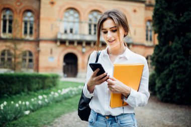 Öğrenci kız smartphone kampüs içinde açık bir şey okumak