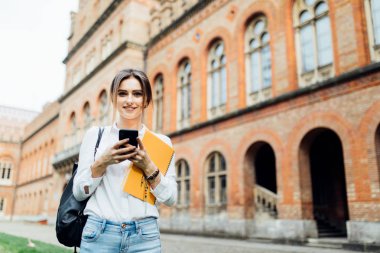 Öğrenci kız smartphone kampüs içinde açık bir şey okumak