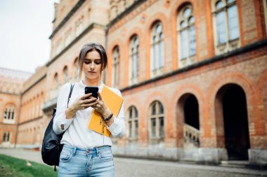 Yürüyüş ve arka planda bina Üniversitesi ile cep telefonu mesajları okuma tek öğrenci