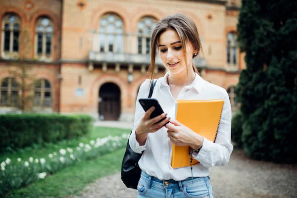 Estudante menina ler algo no smartphone ao ar livre no campus — Fotografia de Stock