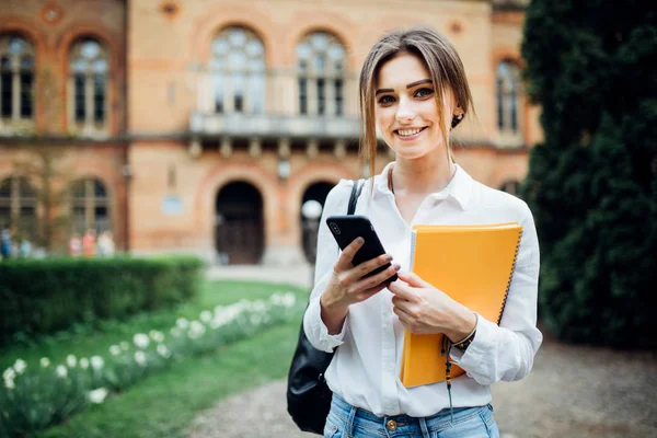 Único estudante andando e lendo mensagens de telefone celular com prédio universitário em segundo plano — Fotografia de Stock