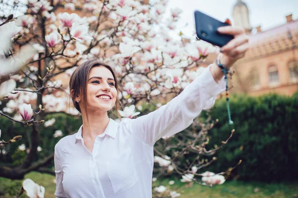 Hermosa mujer caucásica haciendo selfie en flor magnolia jardín . — Foto de Stock