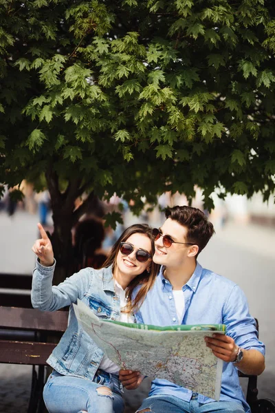 Casal sorridente em óculos de sol com mapa na cidade — Fotografia de Stock