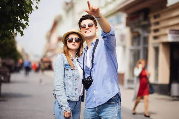 Vacaciones de verano, citas y el concepto de turismo - sonriente pareja en gafas de sol con mapa en la ciudad, el hombre señaló la dirección — Foto de Stock