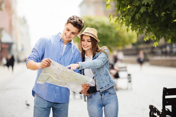 Jóvenes Pareja de turistas está explorando nueva ciudad juntos. Sonriendo y mirar el mapa en la calle de la ciudad — Foto de Stock