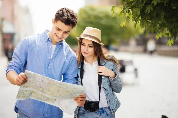 Jeune couple de touristes explore la nouvelle ville ensemble. Souriant et regarder la carte sur la rue de la ville — Photo